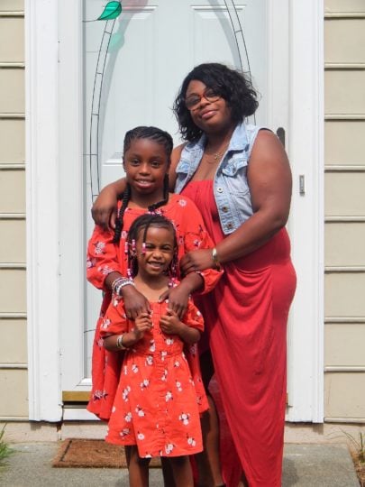 Tonya and her two daughters wearing matching red outfits standing in front of their new home