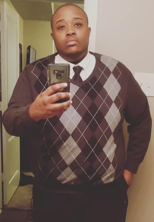 Mirror photo of Davon, pictured wearing a black and gray plaid sweater 